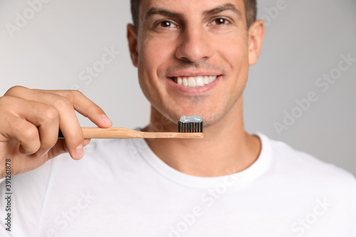 Man holding toothbrush with paste on light background, closeup