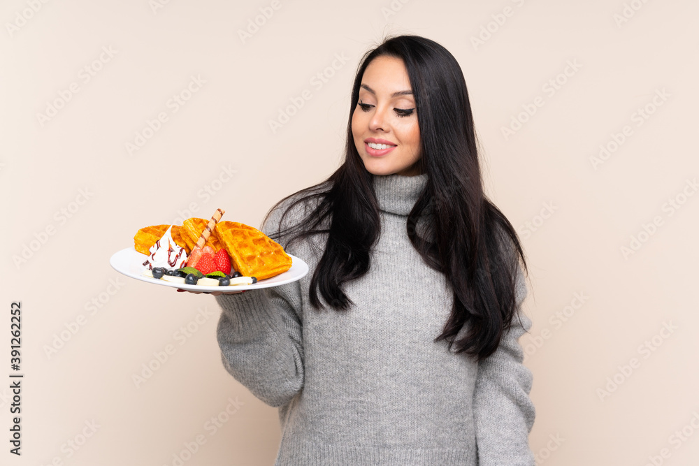 Young Colombian girl holding waffles over isolated background with happy expression Young Colombian girl holding waffles over isolated background with happy expression