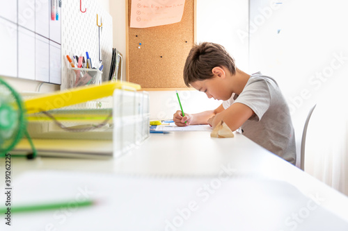 Boy studying and doing homework sitting at his desk in his bedroom at home