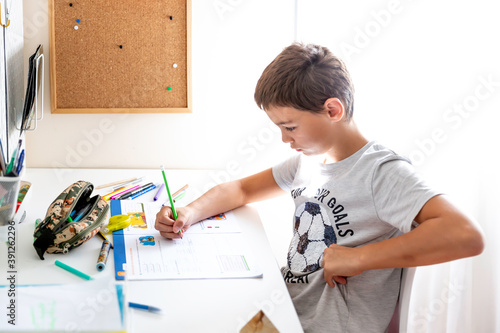 Boy studying and doing homework sitting at his desk in his bedroom at home