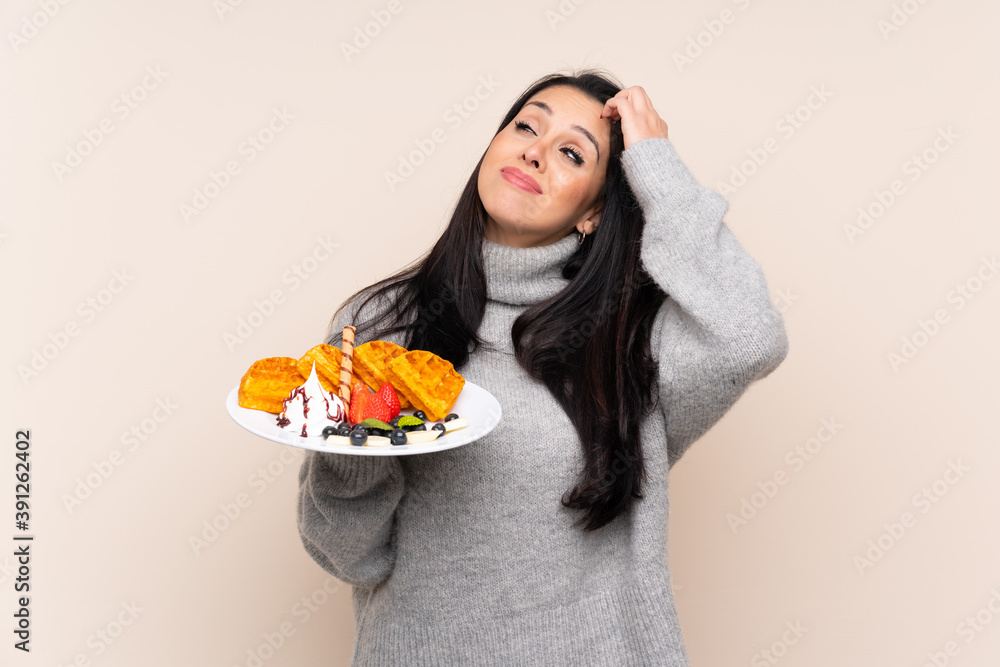 Young Colombian girl holding waffles over isolated background having doubts and with confuse face expression Young Colombian girl holding waffles over isolated background having doubts and with confuse face expression