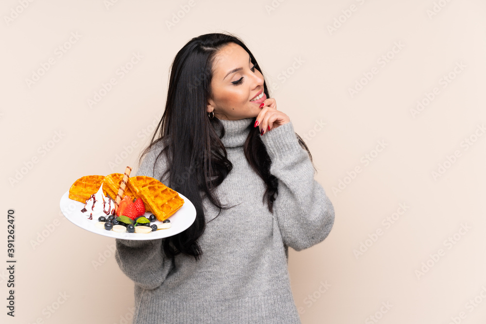 Young Colombian girl holding waffles over isolated background thinking an idea and looking side Young Colombian girl holding waffles over isolated background thinking an idea and looking side
