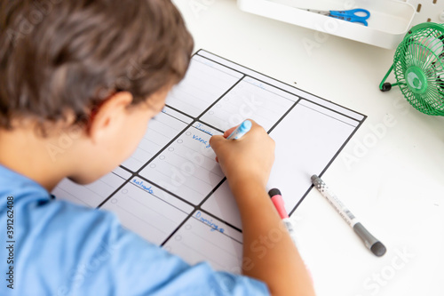 Boy sitting at desk writing with a marker on a weekly planner.
