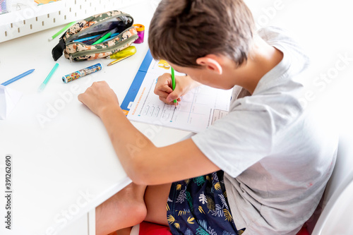 Boy studying and doing homework sitting at his desk in his bedroom at home