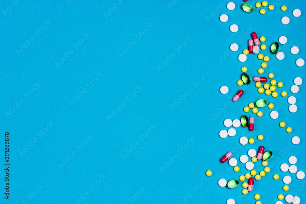 A lot of pharmaceutical capsules, pills, medical tablets are scattered on a blue background. Place for the text. Pharmaceutical frame. View from above