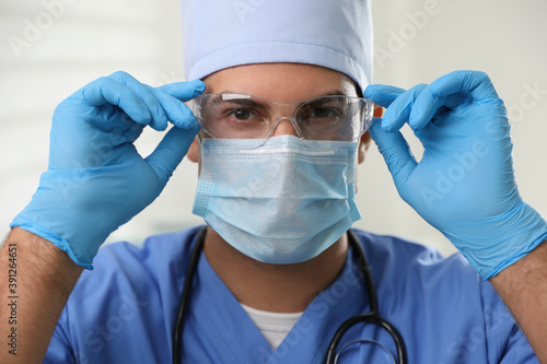 Doctor in protective mask, glasses and medical gloves against light background