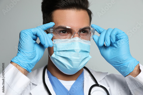 Doctor in protective mask, glasses and medical gloves against light grey background