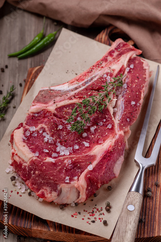 Raw uncooked beef steak. A large piece of meat on the bone lies on a wooden board with spices and fresh herbs.