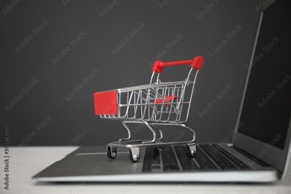 Internet shopping. Laptop with small cart on table against grey background