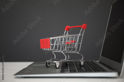 Internet shopping. Laptop with small cart on table against grey background