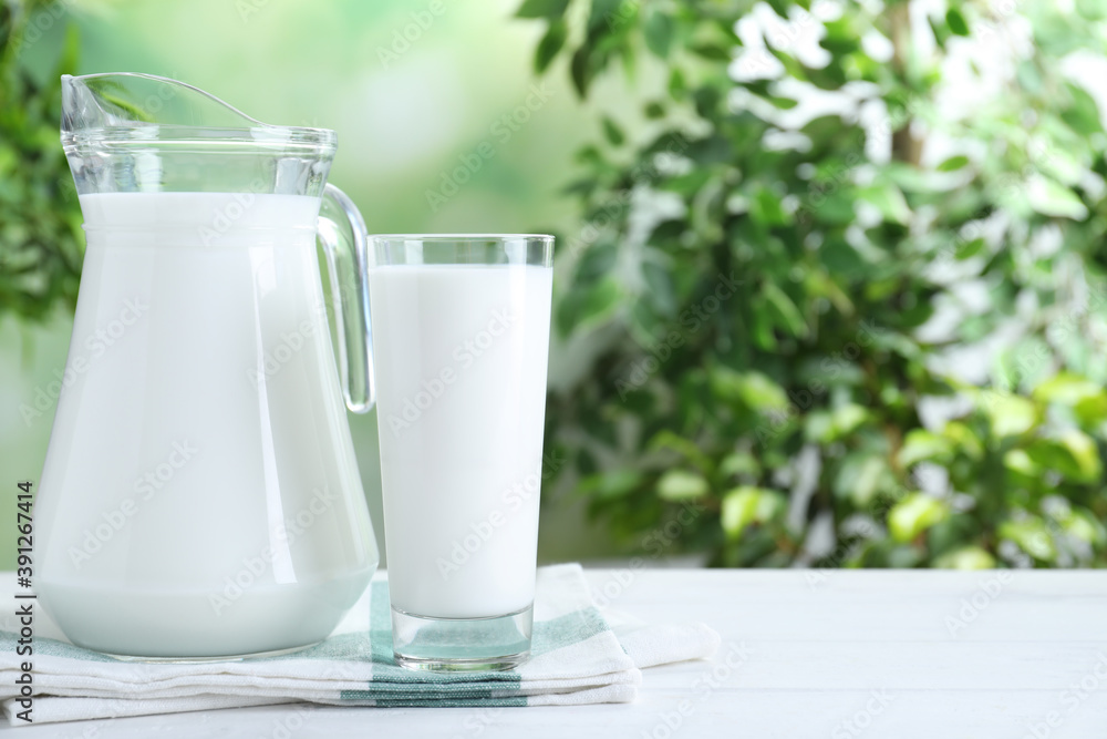 Jug and glass with fresh milk on white wooden table against blurred background. Space for text Jug and glass with fresh milk on white wooden table against blurred background. Space for text