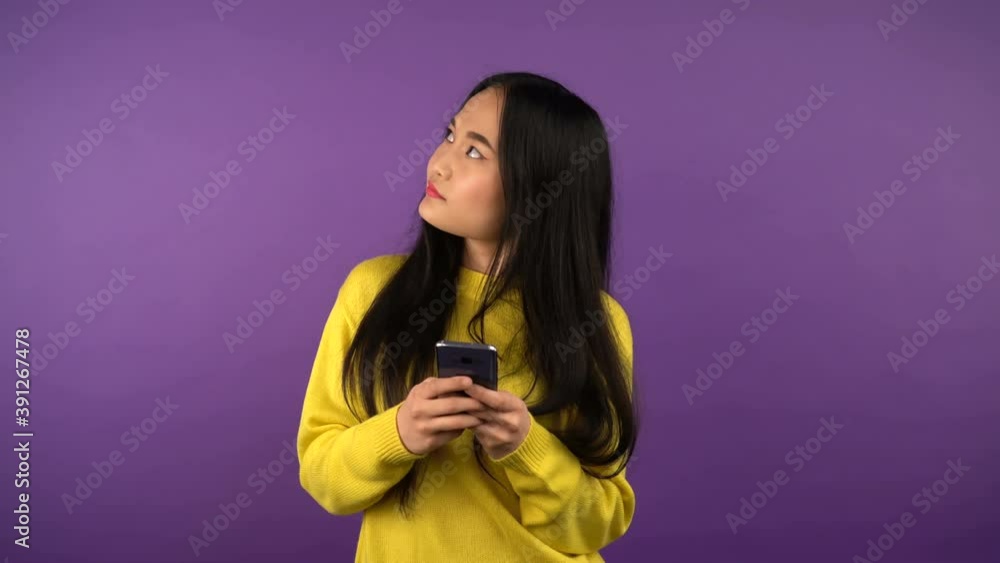 a woman with a smartphone in her hands looks to the right and left while making a choice. isolated purple background. 4K a woman with a smartphone in her hands looks to the right and left while making a choice. isolated purple background. 4K