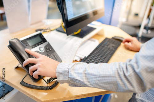 Male customer support operator hand trying to response customer call by using landline phone on working desk in office. Call center business concept photo