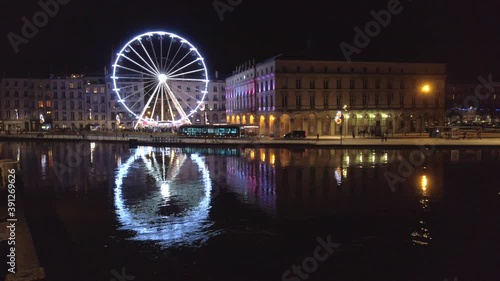 Static shot of the ferris wheel and the town hall at night, with their reflection on the Nive river, Bayonne, France.
