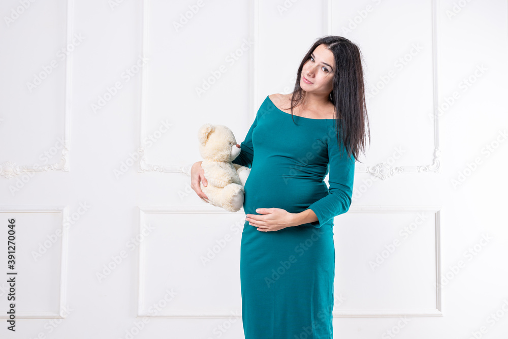 A pregnant girl in a dress with a teddy bear in her hands.