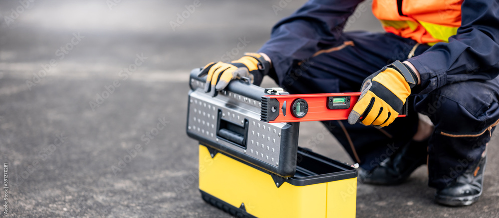 Male mechanic or maintenance worker man holding red aluminium spirit level tool or bubble levels opening tool box at construction site. Equipment for civil engineering project
