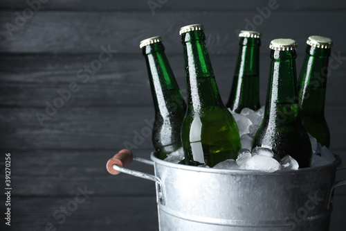 Metal bucket with bottles of beer and ice cubes on dark wooden background, closeup. Space for text