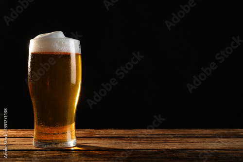Cold tasty beer on wooden table against dark background. Space for text