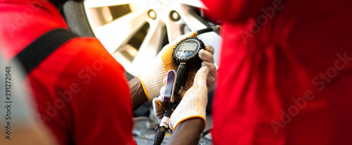 Closu up black mechanic inflating a tire in service station. checking air pressure with gauge. Car maintenance and auto service garage concept. photo