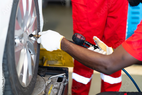 Closu up black mechanic inflating a tire in service station. checking air pressure with gauge. Car maintenance and auto service garage concept. photo