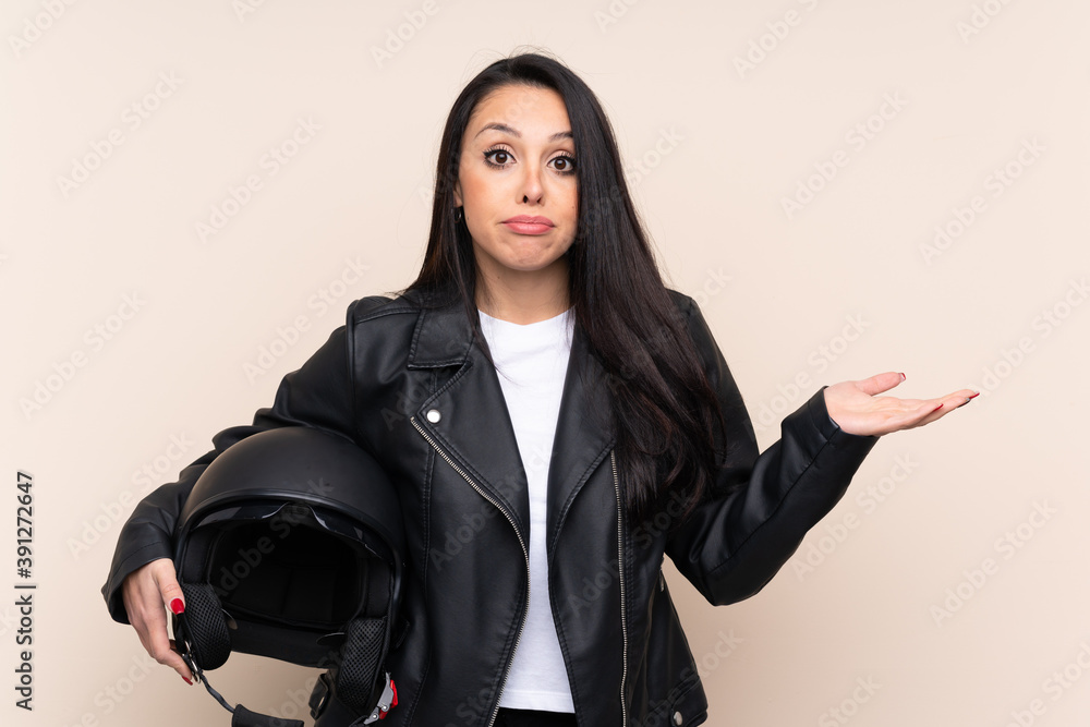 Young Colombian girl holding a motorcycle helmet over isolated background having doubts with confuse face expression Young Colombian girl holding a motorcycle helmet over isolated background having doubts with confuse face expression