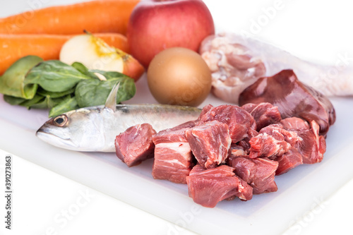 Closeup of ingredients of barf raw food recipe for dogs consisting meat, organs, fish, eggs and vegetable on chopping board