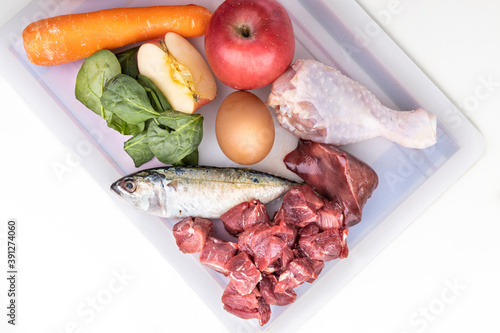 Overhead view of ingredients of barf raw food recipe for dogs consisting meat, organs, fish, eggs and vegetable on chopping board photo