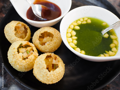 Panipuri, famous street food in Pakistan, India and Bangladesh. Other names are fuchka, gupchup or golgappa. Made from deep-fried crispy filled with mash potato. Dip with green sauce (imli pani). photo