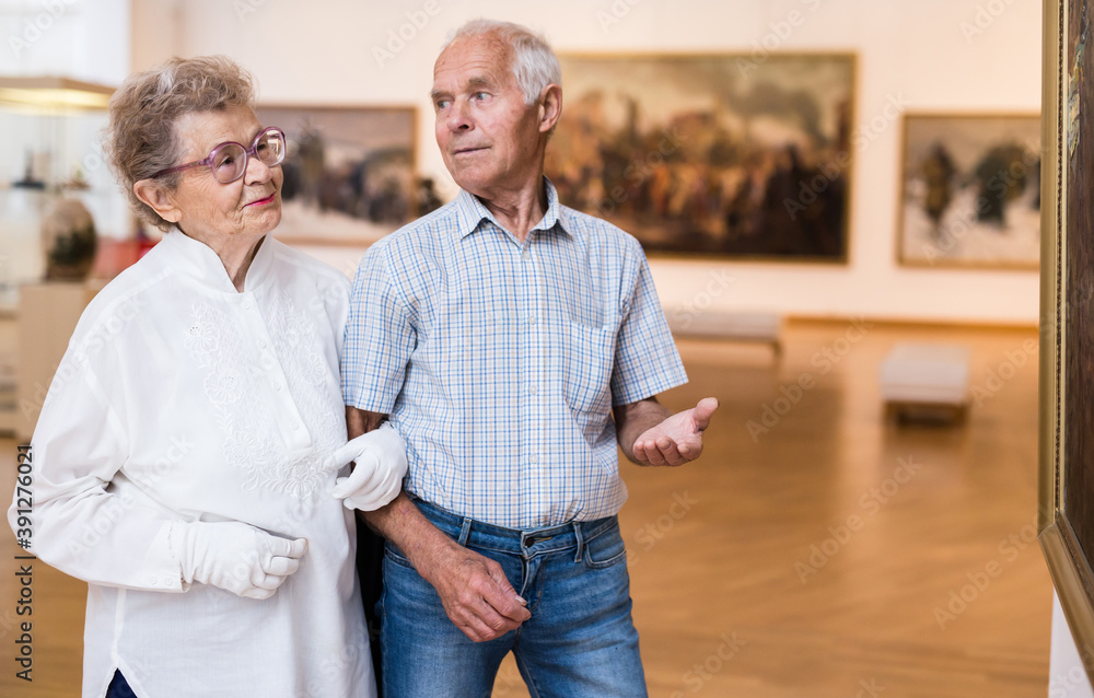 mature European couple examines paintings in an exhibition in hall of art museum mature European couple examines paintings in an exhibition in hall of art museum