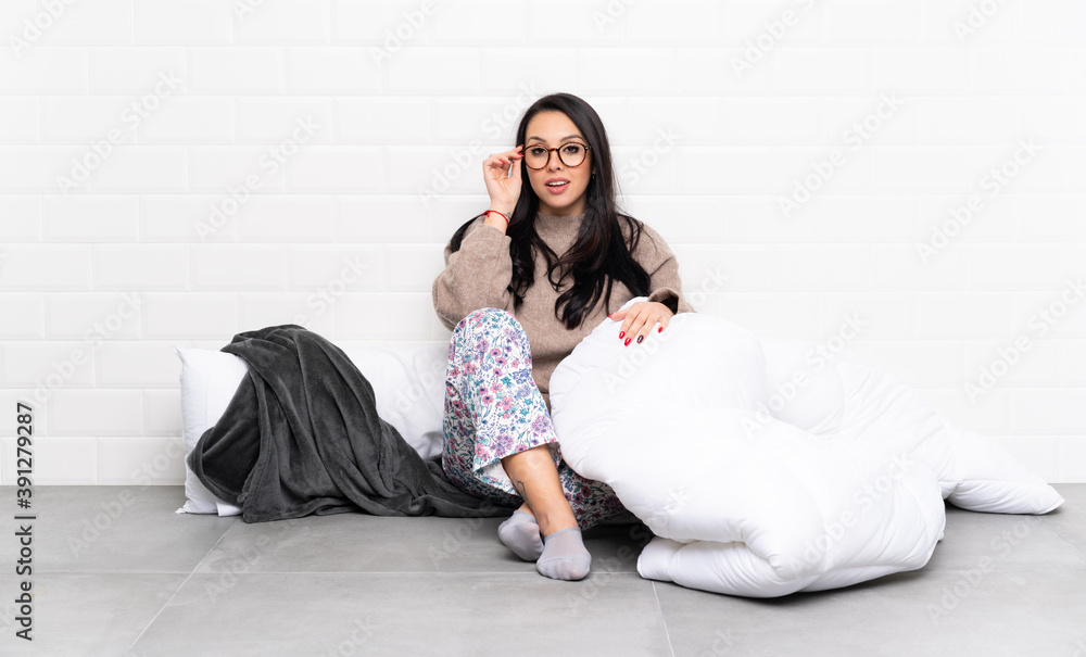 Young Colombian girl in pajamas at indoors with glasses and surprised Young Colombian girl in pajamas at indoors with glasses and surprised