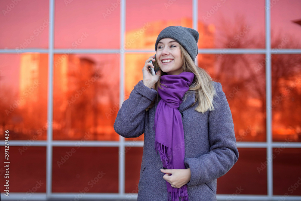 Happy casual woman says a message to messengers stands on the street warmly a bright red background. Social Media Managernegotiates with customers by phone during business hours