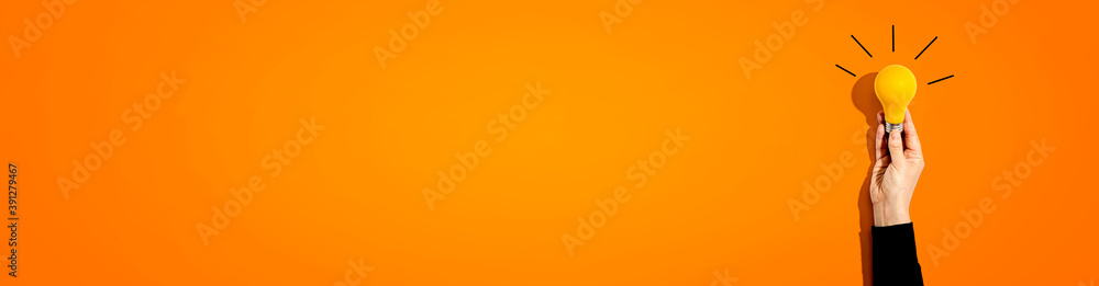 Person holding a yellow light bulb - Idea and creativity theme Person holding a yellow light bulb - Idea and creativity theme