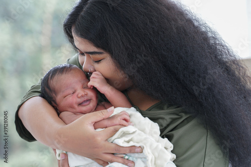 Portrait of African mom carrying and kiss adorable newborn baby in her arm. Happy lovely African American family mother and son at bedroom