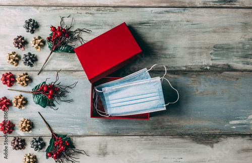 Christmas ornaments and face masks in gift box on wooden background. Covid-19 and holiday concept.