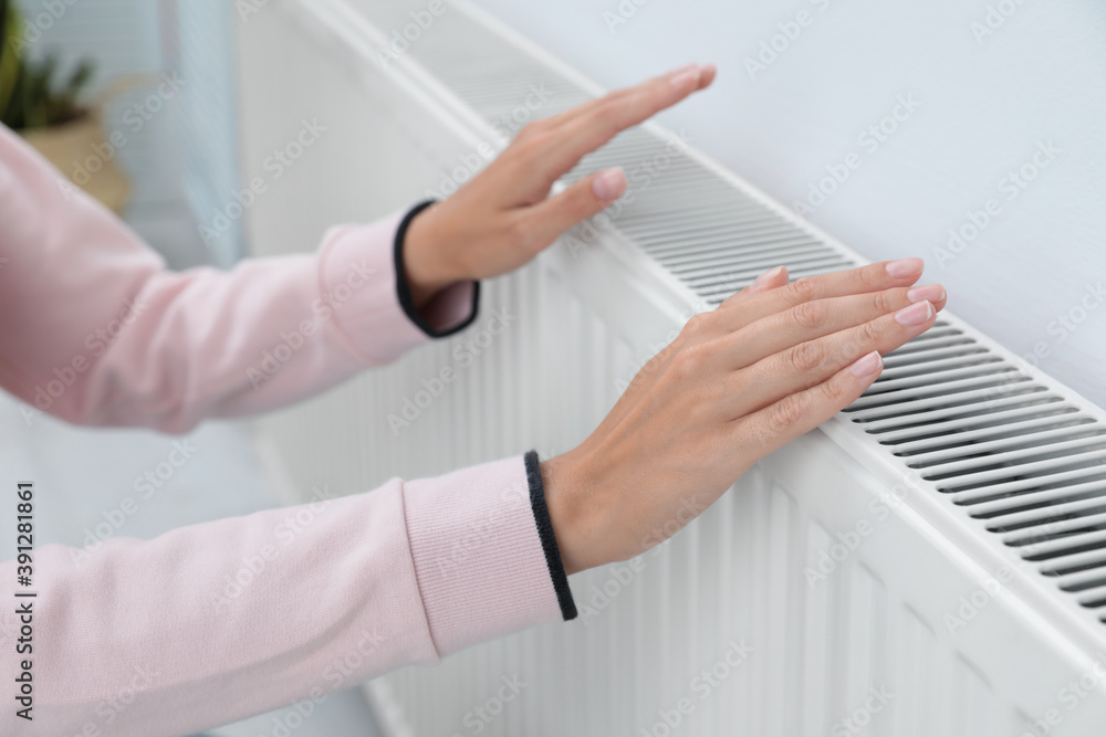 Obraz premium Woman warming hands on heating radiator near white wall, closeup