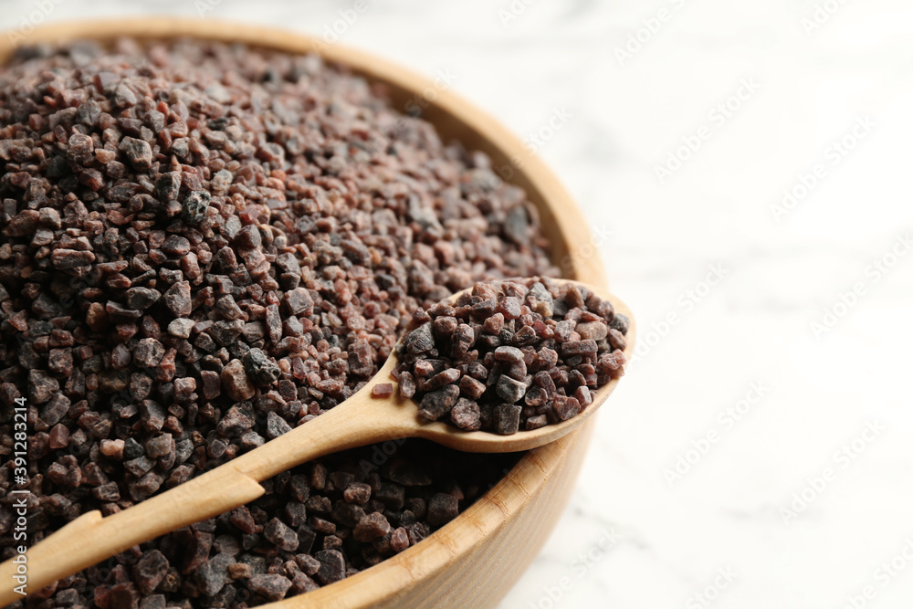 Black salt in bowl with spoon on white table, closeup. Space for text Black salt in bowl with spoon on white table, closeup. Space for text