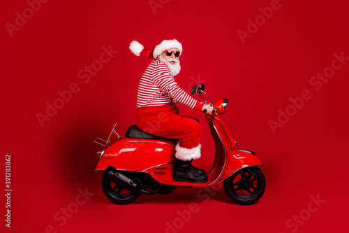 Full length profile photo of retired grandpa scooter ride highway road fast carefree wear santa x-mas costume suspenders sunglass boots striped shirt cap isolated red color background