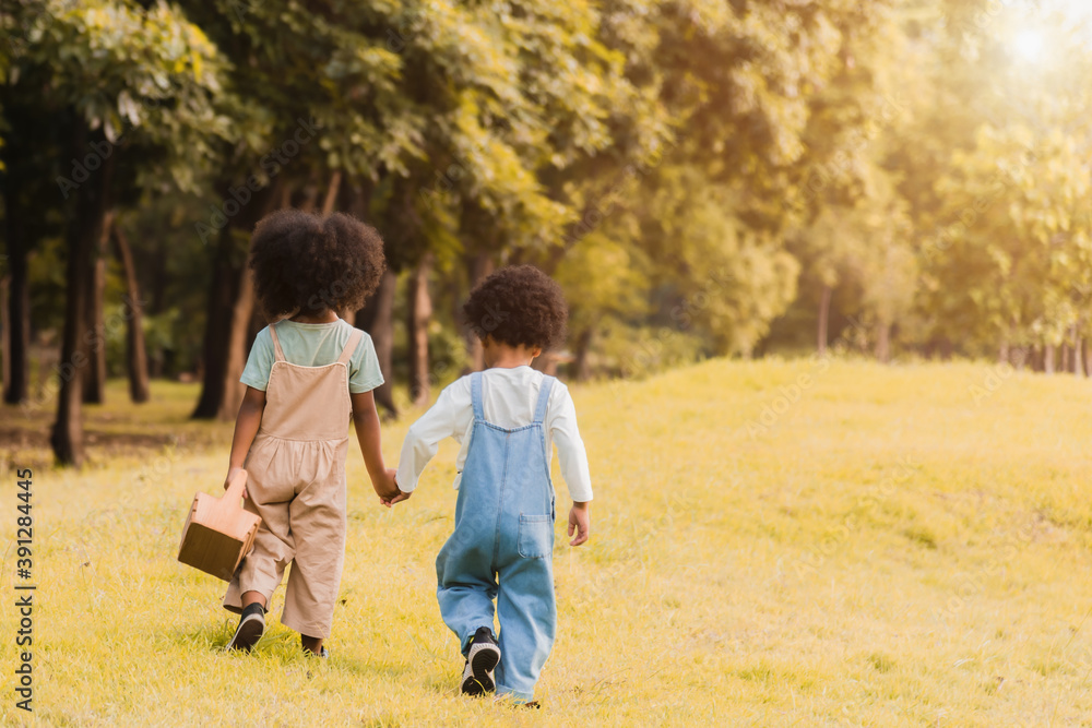 Back view of two adorable african children, girl and boy holding hand and walking together in garden. Back view of two adorable african children, girl and boy holding hand and walking together in garden.