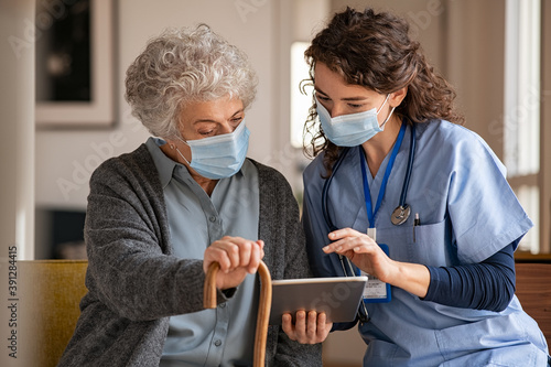 Senior woman and nurse using digital tablet at home during consult photo