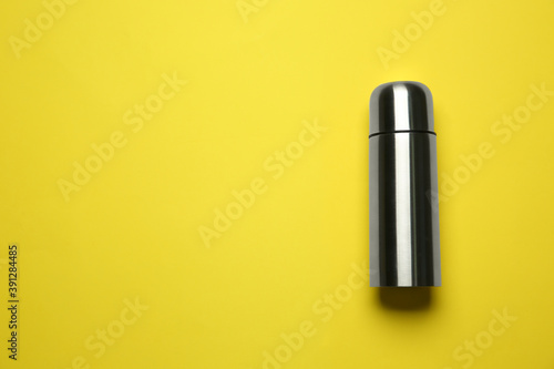 Stainless steel thermos on yellow background, top view. Space for text
