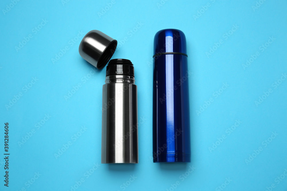 Stainless steel thermoses on light blue background, flat lay