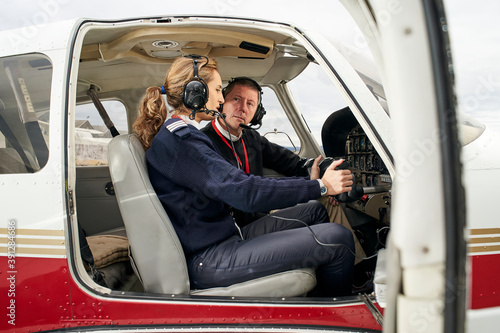 Pilot in training and flight instructor in the cockpit of an airplane. Female pilot with headphones preparing to fly. He is sitting next to the female instructor attending to her explanations.