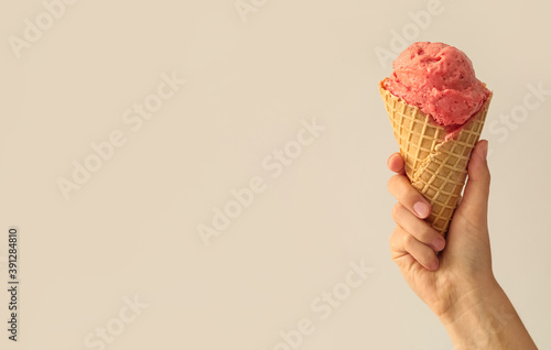 Woman holding waffle cone with delicious pink ice cream on white background, closeup. Space for text