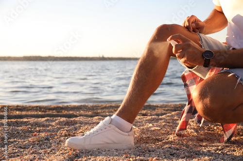 Man using insect repellent near sea on sunny day, closeup photo