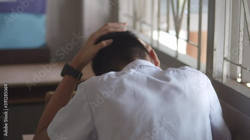 A male high school student in white uniform  is sitting alone, being so tense that he crunched his head in the classroom.