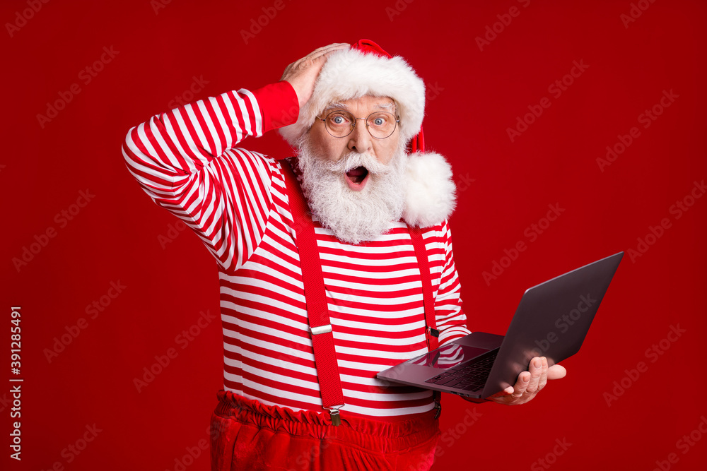 © deagreez - Photo of retired grandfather grey beard hold laptop shock hand head forget fulfill kid wish wear santa x-mas costume suspenders spectacles striped shirt cap isolated red color background