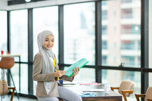 Asian Muslim businesswoman in hijab head scarf working with paper document in the modern office. businesspeople, diversity and office concept photo
