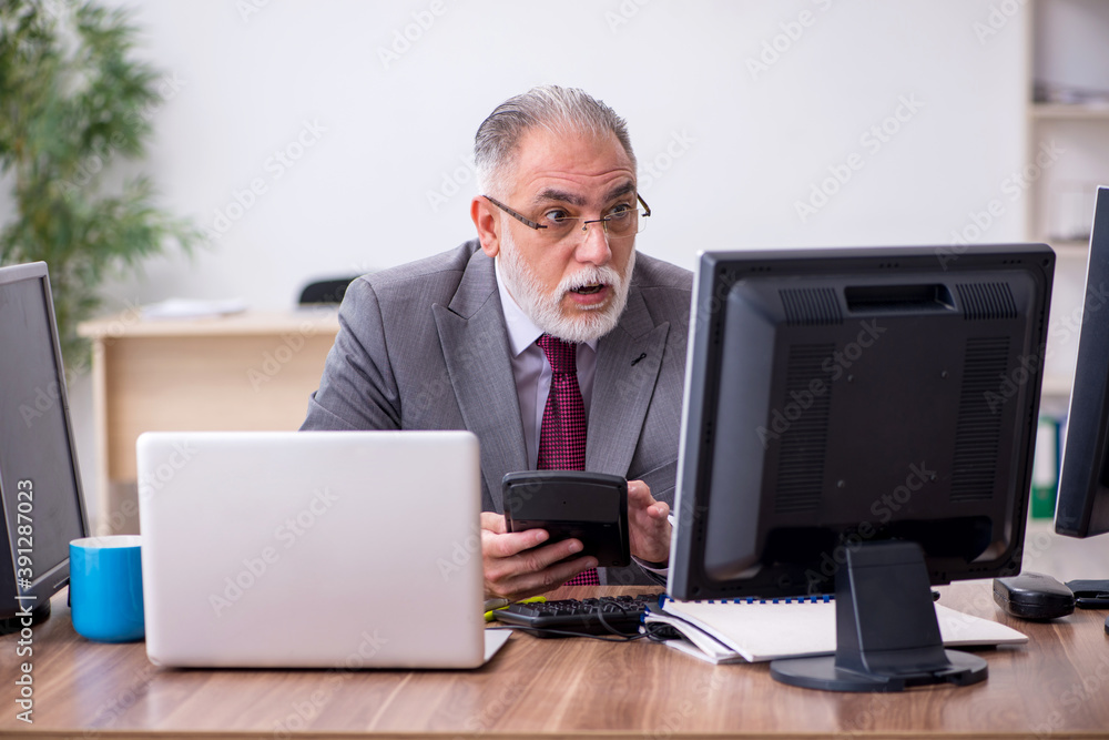 Old male boss sitting at desktop in the office Old male boss sitting at desktop in the office