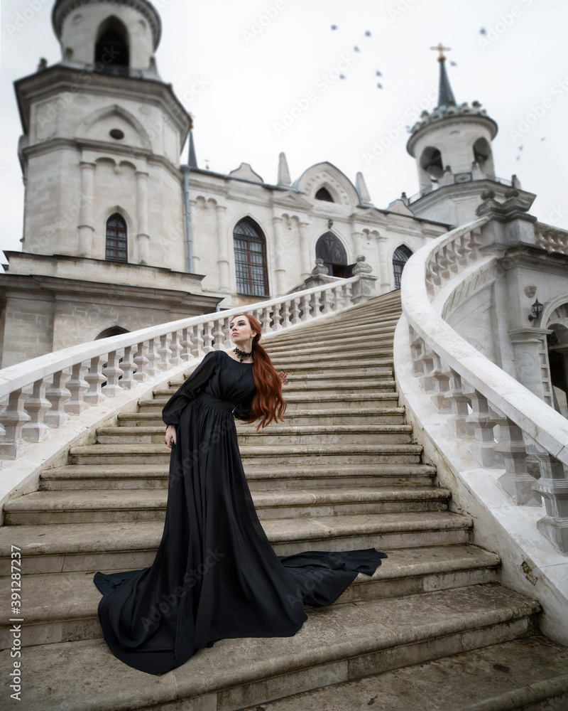 Art photo of a red-haired woman in a black dress on the steps of a gothic temple