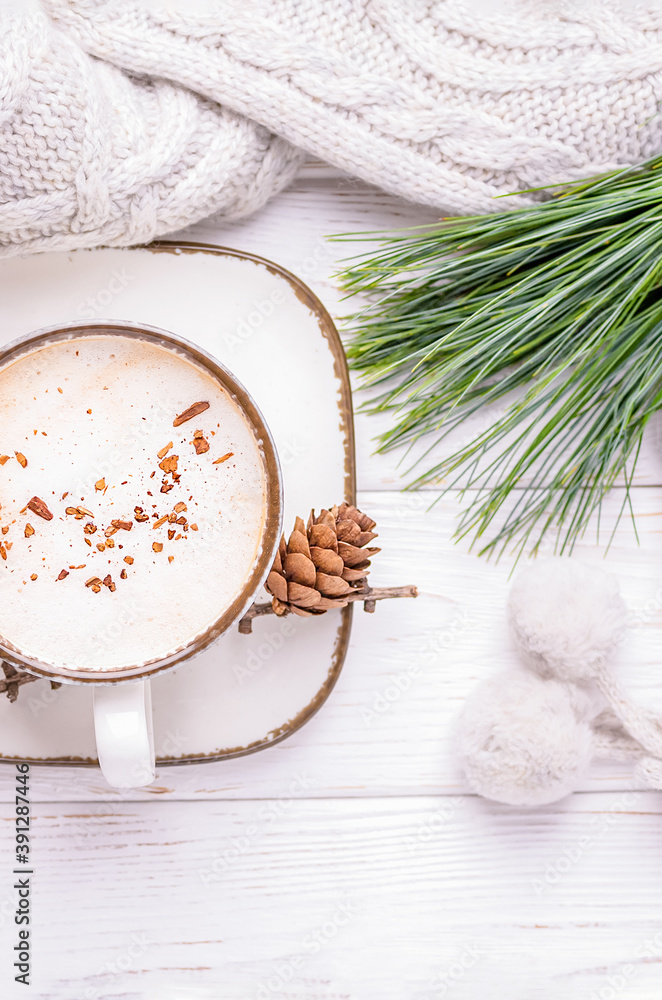 Fototapeta premium Cappuccino with cinnamon, a branch of a pine tree and knitted accessories on a white wooden background